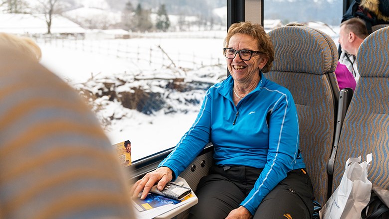 Eine Reise in das winterliche Mariazellerland ist bequem und einfach zu erreichen., © NÖVOG/Grojer Frau sitzt im Zur bei winterlicher Landschaft.