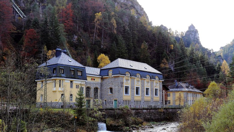 Das EVN Kraftwerk Wienerbruck, © EVN Kraftwerk Wienerbruck/Raimo Rumpler Gelbes Kraftwerkgebäude mit grauem Dach an Flussufer, umgeben von herbstlichen Bäumen und Felsen.