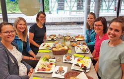 Gruppe von Frauen beim gemeinsamen Frühstück an einem langen Tisch.