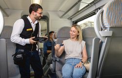 Zugbegleiter kontrolliert das Ticket einer Reisenden im Zug.