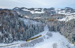Mariazellerbahn fährt durch eine tief verschneite Wald- und Hügellandschaft.