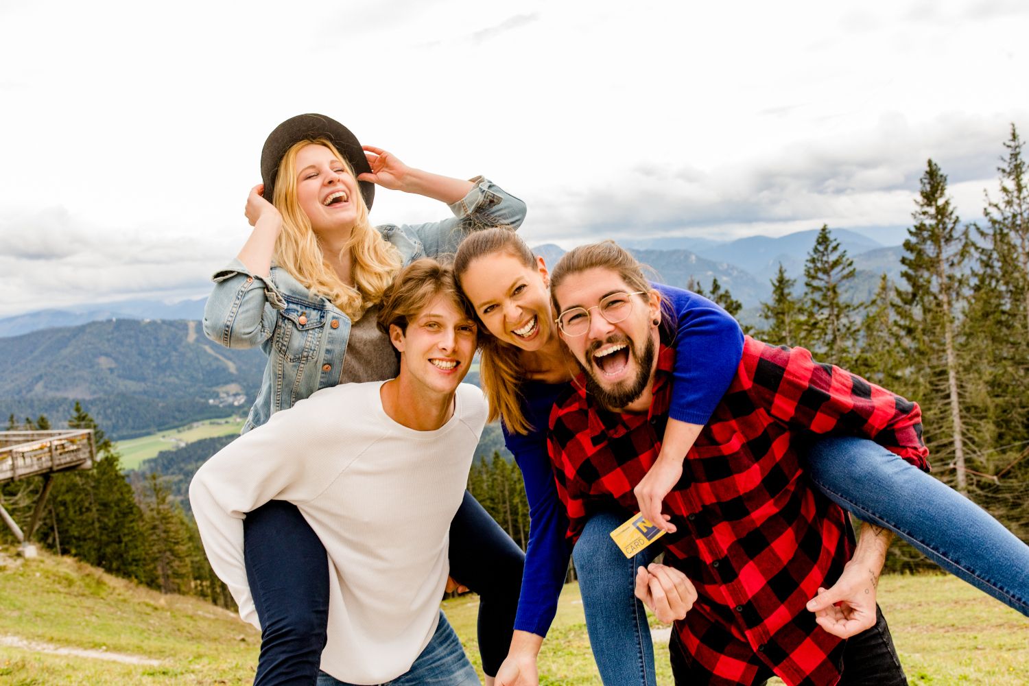 Vier lachende Personen in Berglandschaft, zwei tragen die anderen auf dem Rücken.