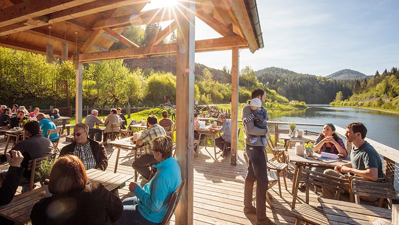 Menschen sitzen auf Bistroterrasse neben Gewässer