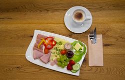 Frühstücksteller mit Schinken, Käse, Gemüse und einer Tasse Kaffee.