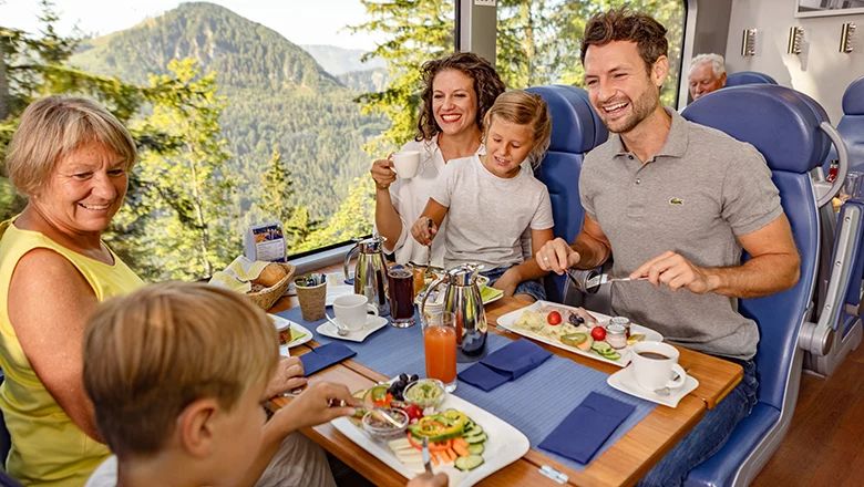 Eine Familie sitzt im Panoramawagen der Bahn an einem gedeckten Tisch und frühstückt gemeinsam.