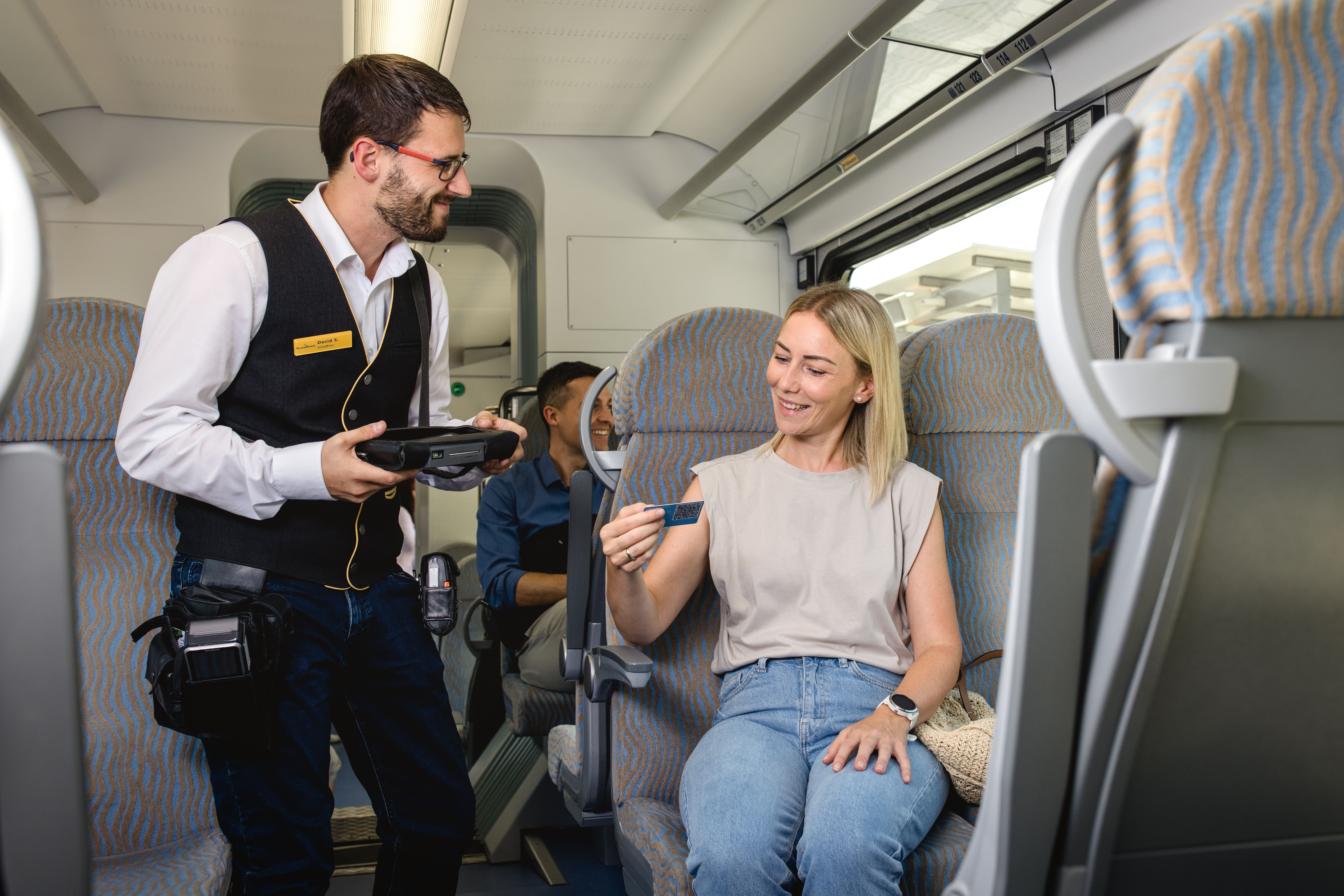 Zugbegleiter kontrolliert das Ticket einer Reisenden im Zug.