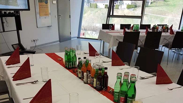 Festlich gedeckte Tische mit Getränken und roten Servietten in einem Veranstaltungsraum.