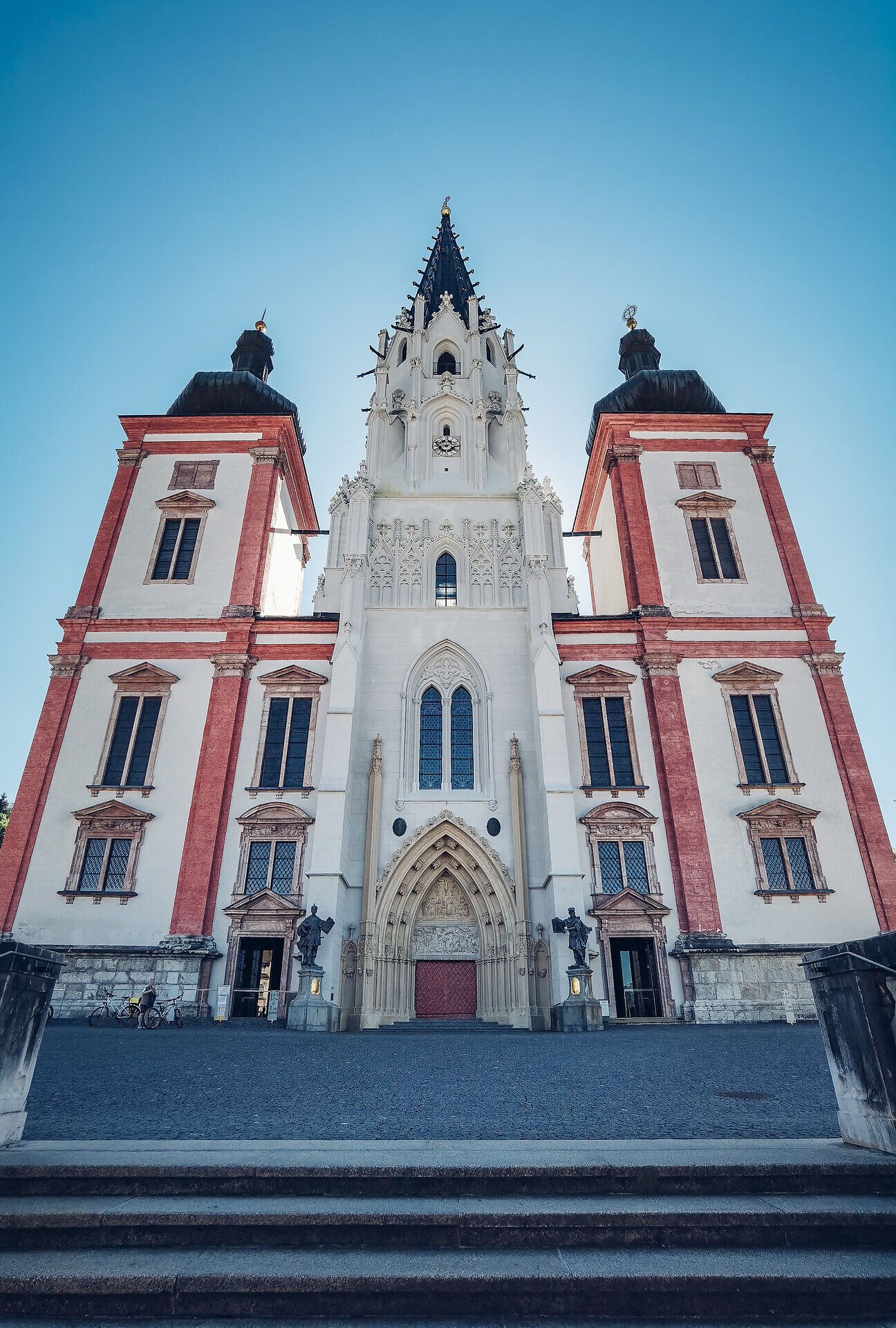 Die majestätische Wallfahrtsbasilika erhebt sich stolz gegen den klaren Himmel und zieht mit ihrer beeindruckenden Architektur die Blicke der Besucher an. Umgeben von sanften Hügeln und üppigem Grün, bietet dieser Ort eine friedliche Atmosphäre, die zum Verweilen und Staunen einlädt.