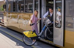 Eine Frau verlädt zusammen mit einem Zugbegleiter ein Fahrrad durch die geöffnete Tür in einen Zug.