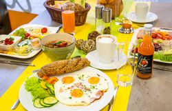 Reich gedeckter Frühstückstisch mit Eiern, Gemüse, Brot, Säften und Heißgetränken.
