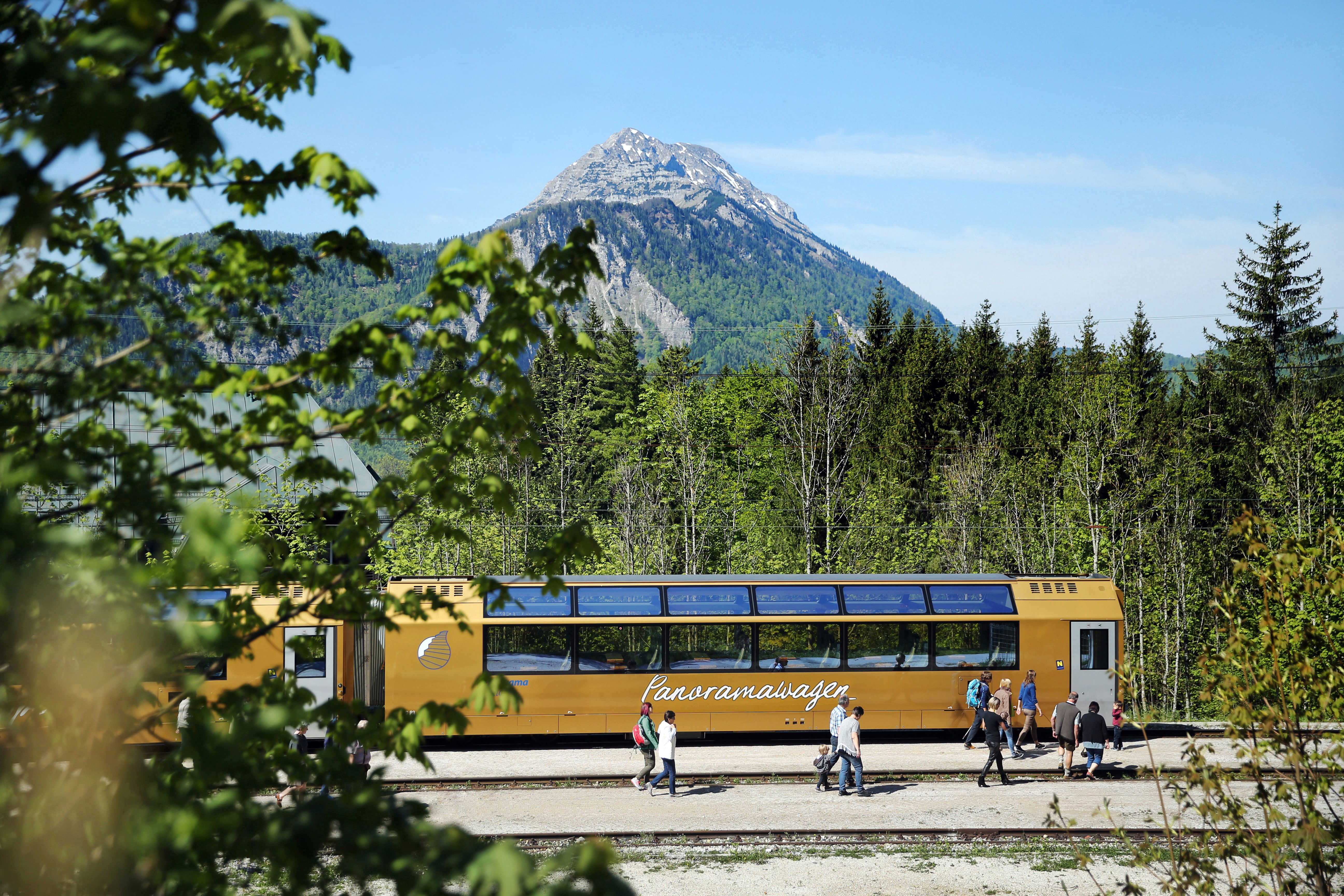 Goldener Panoramawagen der Mariazellerbahn vor der Bergkulisse "Ötscher"mit Menschen auf dem Bahnsteig.