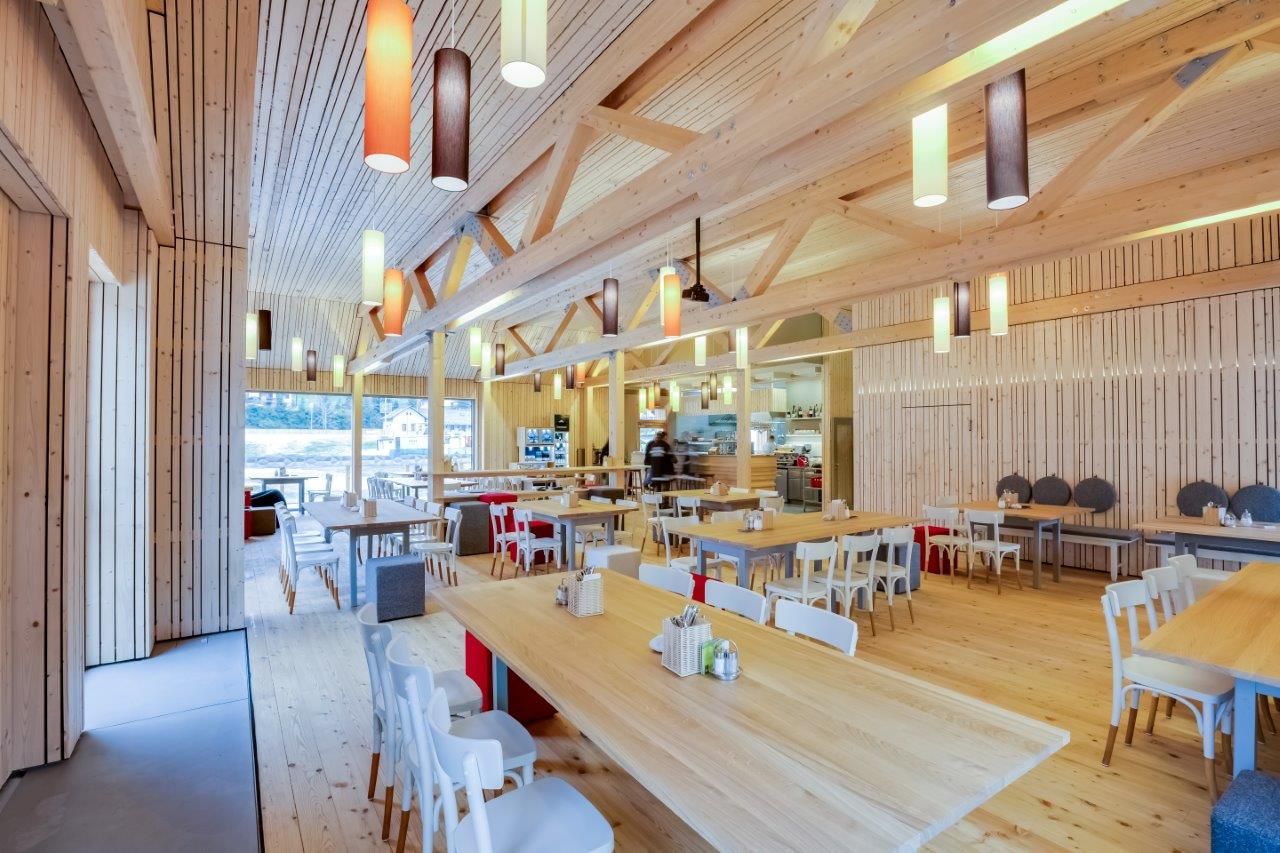 Innenansicht eines modernen Restaurants mit Holzmöbeln und bunten Hängelampen.