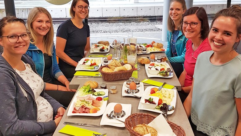 mehrere Personen sitzen bei gedecktem Frühstückstisch im Bistro