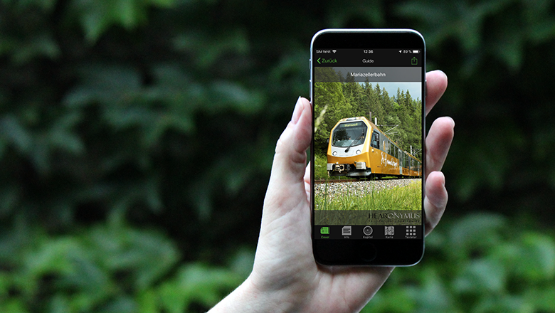 jemand hält ein Handy in der Hand auf dem ein Foto der Mariazellerbahn geöffnet wurde