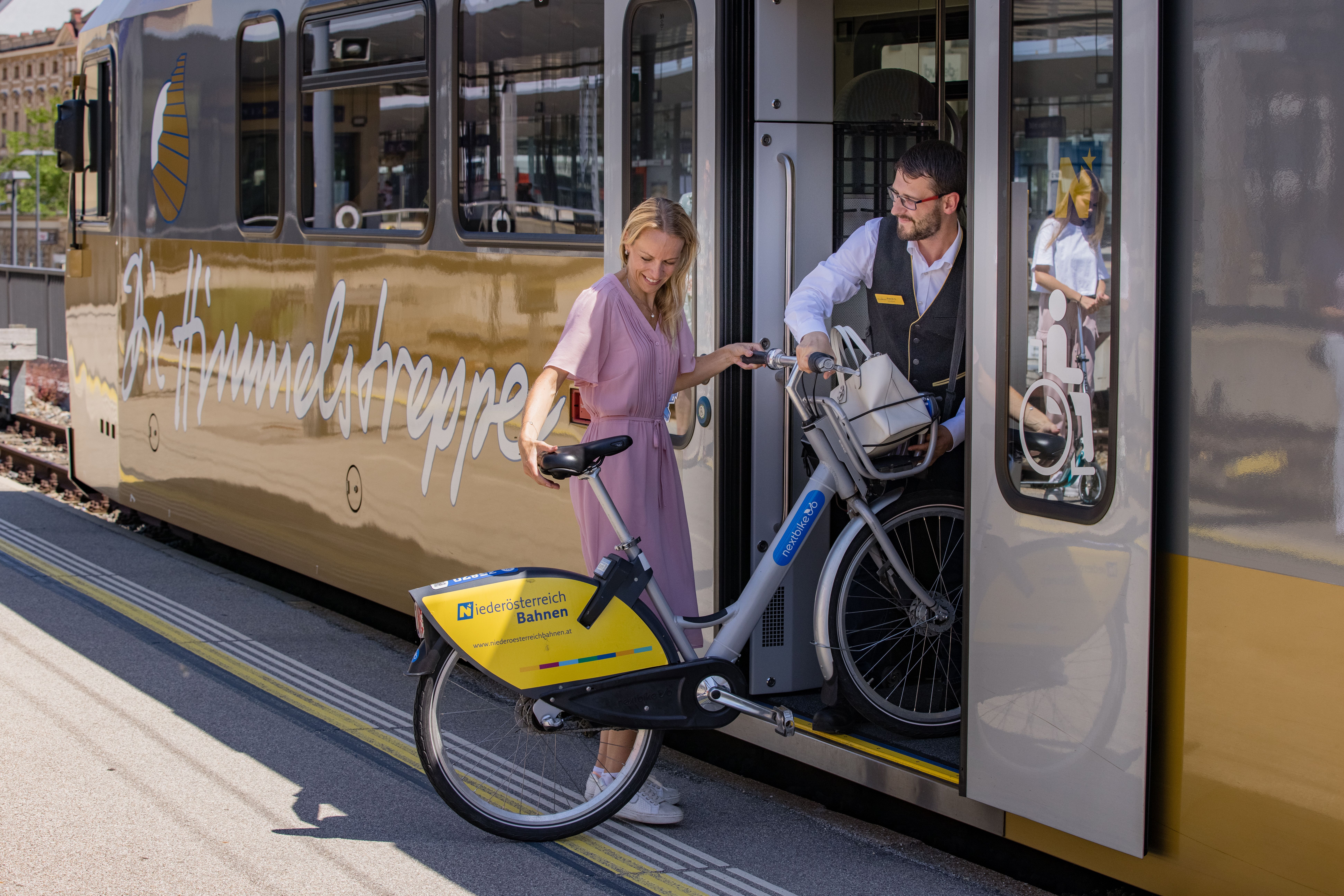 Eine Frau verlädt zusammen mit einem Zugbegleiter ein Fahrrad durch die geöffnete Tür in einen Zug.