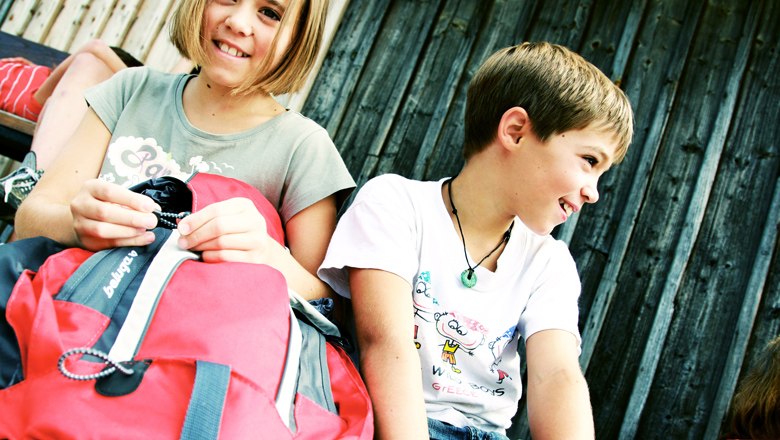 zwei Kinder lachen und halten Wanderrucksack in der Hand