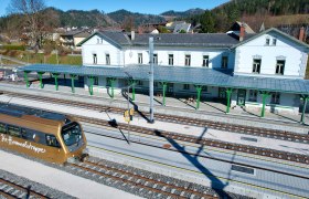 Bahnhof mit Zug und umliegender Landschaft.