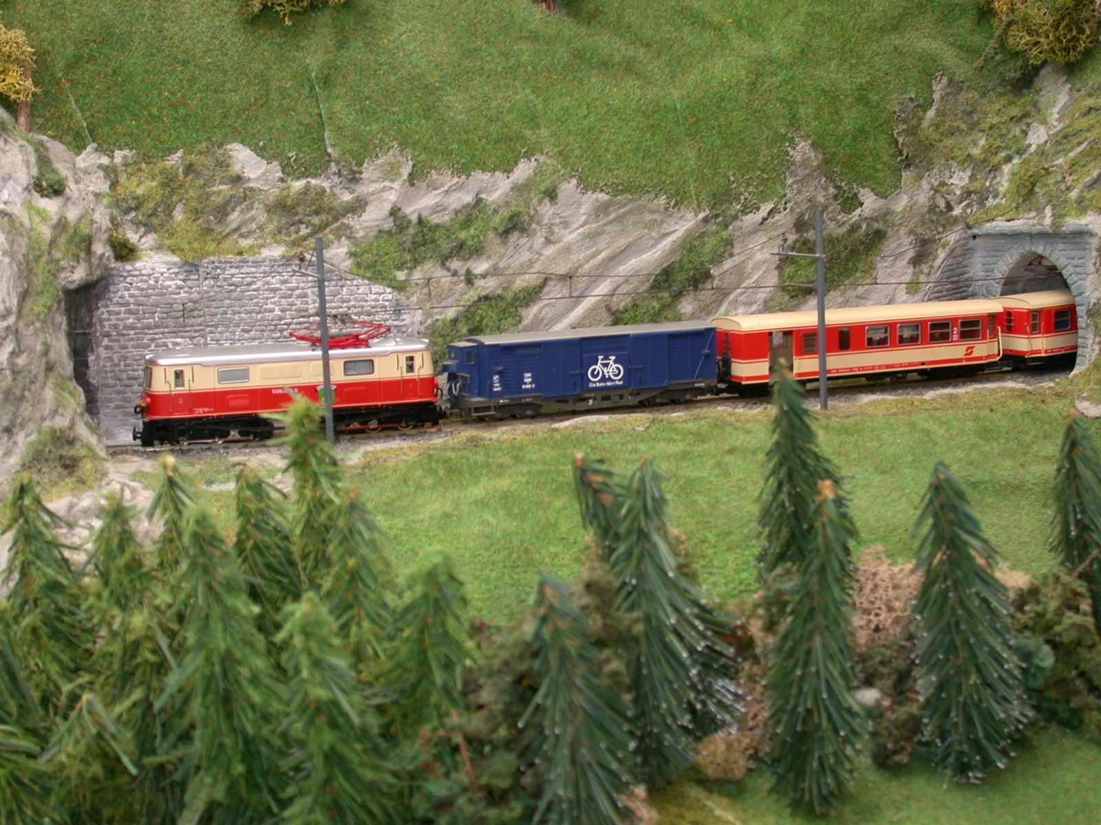 Modellbahnzug fährt durch eine Tunnelöffnung in einer Miniaturlandschaft mit Bäumen und Felsen.