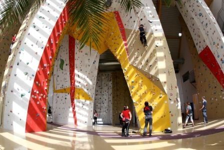 Innenansicht einer Kletterhalle mit bunten Kletterwänden und mehreren Personen beim Klettern.