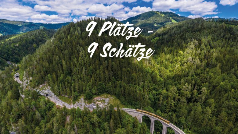 Bahn fährt über ein Viadukt durch bewaldete Berge unter blauem Himmel mit Wolken, Text '9 Plätze - 9 Schätze' in der Bildmitte