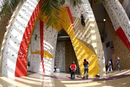 Interior view of a climbing hall with colorful climbing walls and several people climbing.
