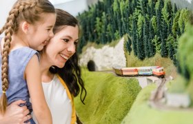 Mutter und Kind schauen sich Modelleisenbahn an