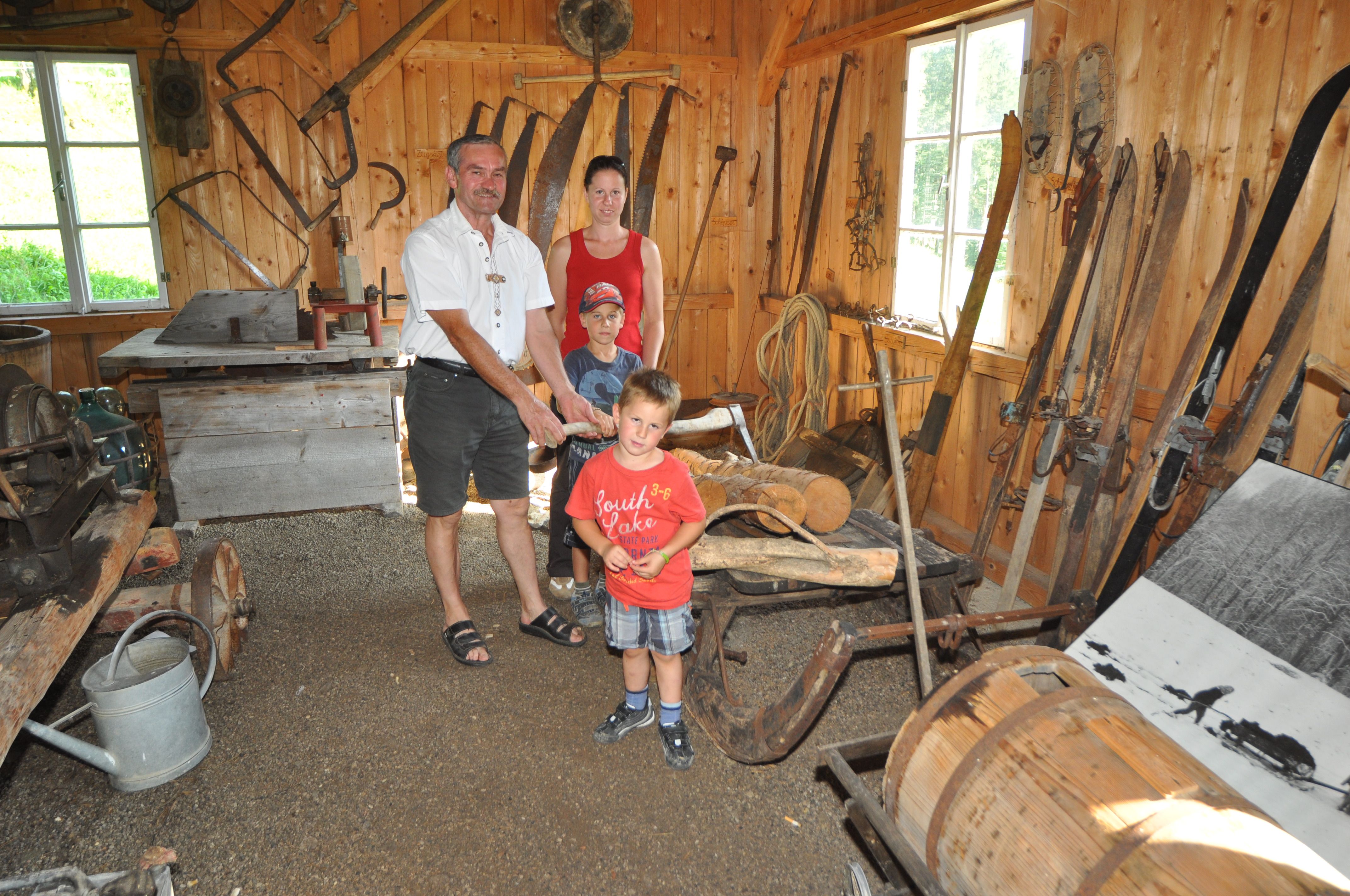 Familie in traditioneller Holzhütte mit alten landwirtschaftlichen Geräten.