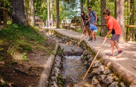 Familie spielt mit St&ouml;cken in einem Wasserkanal im Wald.