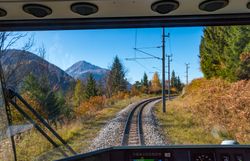 Blick aus dem Führerstand eines Zuges auf eine kurvige Bahnstrecke durch herbstliche Landschaft mit Bergen und Bäumen