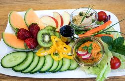 Bunte Obst- und Gemüseplatte mit verschiedenen Aufstrichen.