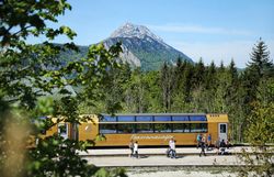 Goldener Panoramawagen der Mariazellerbahn vor der Bergkulisse "Ötscher"mit Menschen auf dem Bahnsteig.