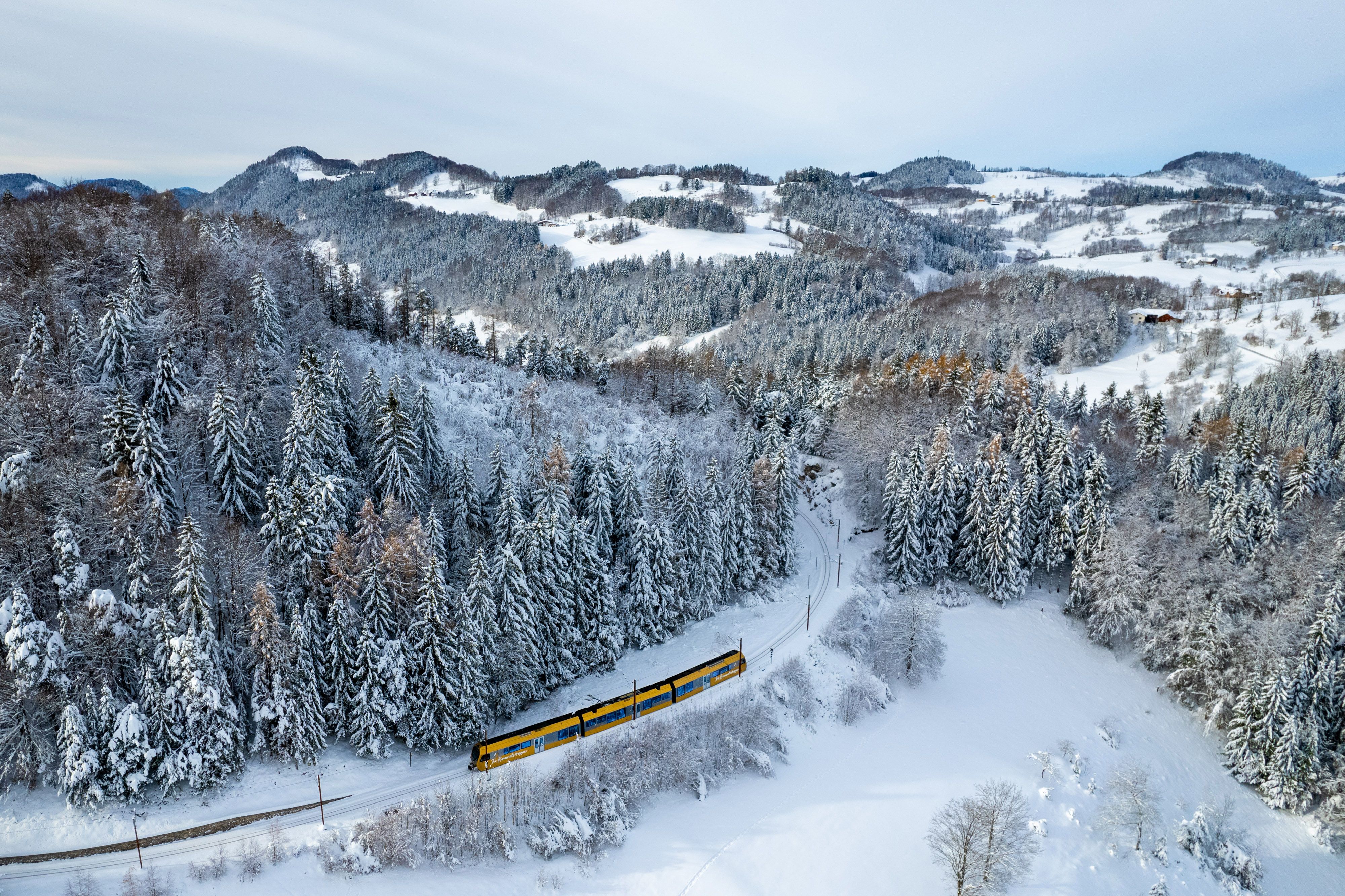 Mariazellerbahn fährt durch eine tief verschneite Wald- und Hügellandschaft.